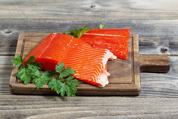 Fresh Red Salmon on Wooden Server Horizontal photo of fresh raw red salmon fillet on traditional wooden server with parsley on the side and rustic wood underneath sockeye salmon filet stock pictures, royalty-free photos & images