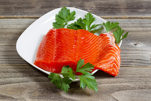 Closeup horizontal photo of fresh red salmon fillet on white plate with parsley on the side and rustic wood underneath