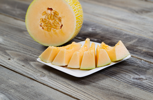 Closeup view of a freshly cut melon with slices on white plate and half of melon in background on rustic wood