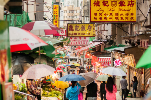 Hong Kong iStockalypse.  Shoppers with umbrellas walk through a busy outdoor food market in Sheung Wan District, Hong Kong, China