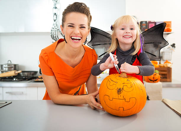 istock Mother with halloween dressed daughter creating Jack-O-Lantern 500540680