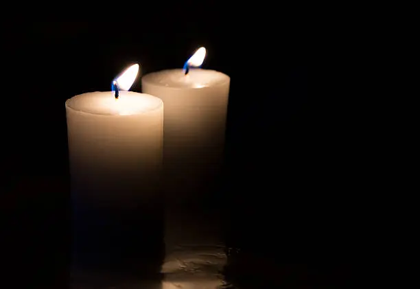 two white candles burn in the dark 
