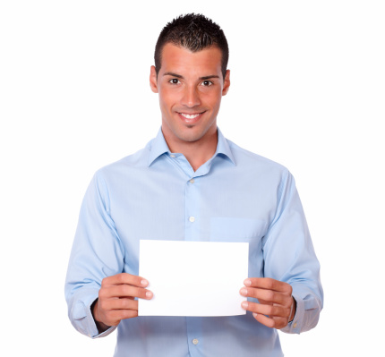 Portrait of an attractive latin guy holding a white card while standing and smiling at you on isolated background - copyspace