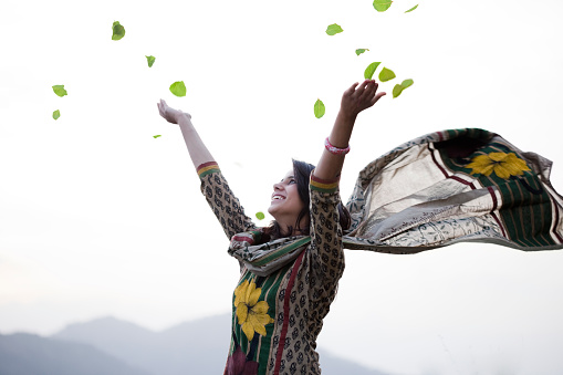 Happy young woman flying leafs in air towards sky.