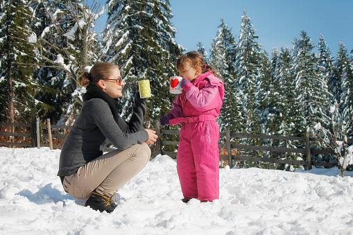 The little girl and her mother enjoy the snow and they drink tea.