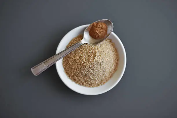 top view of a pile of cane-sugar and a spoon of ground coffee in the grey background