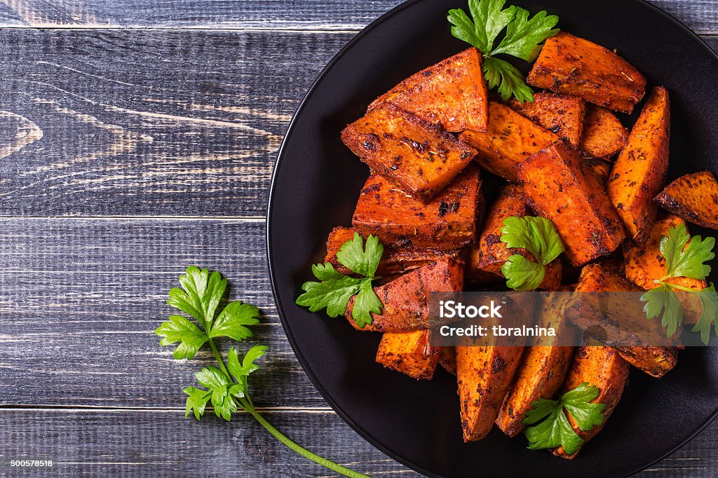 Homemade Cooked Sweet Potato with spices and herbs. Homemade Cooked Sweet Potato with spices and herbs on dark background. French Fries Stock Photo