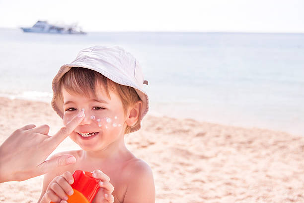 main de la mère appliquer suncream à son fils sur la plage. - water child bottle little boys photos et images de collection