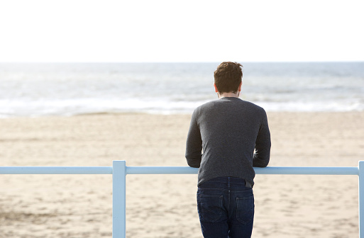 Portrait from behind of a young man standing alone looking at the sea