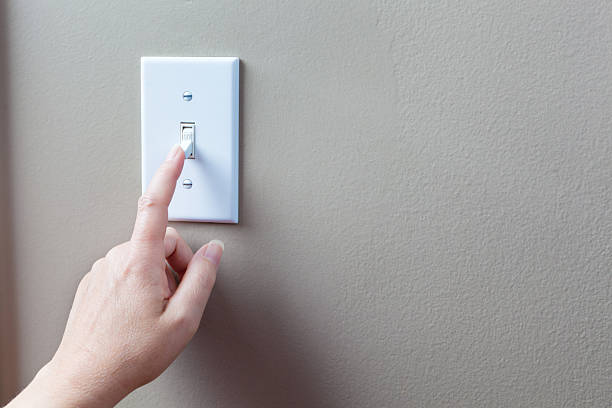 Conserving Eletricity Energy by Turning Off Light Switches Horizontal Hand on light switch turning off light to conserve electricity. light switch stock pictures, royalty-free photos & images