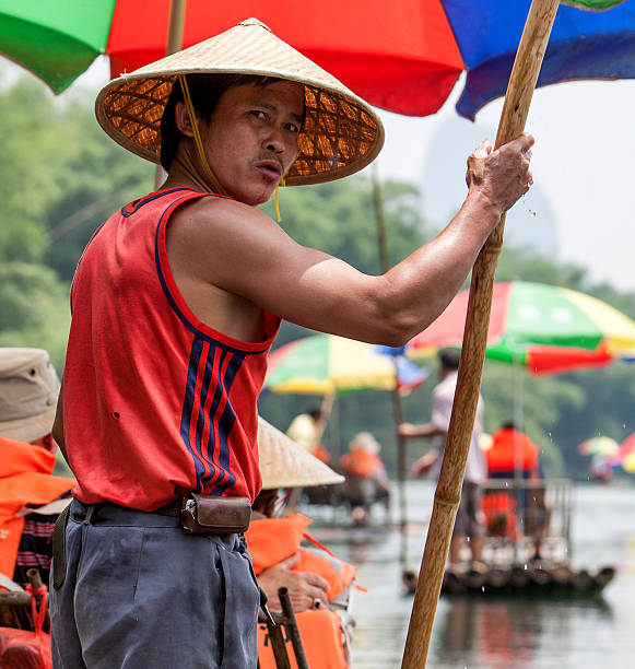 Li River, near Guilin, China- May 25 2010: A Chinese man rides a bamboo boat with tourists on Li River in China with a long pole Bamboo.