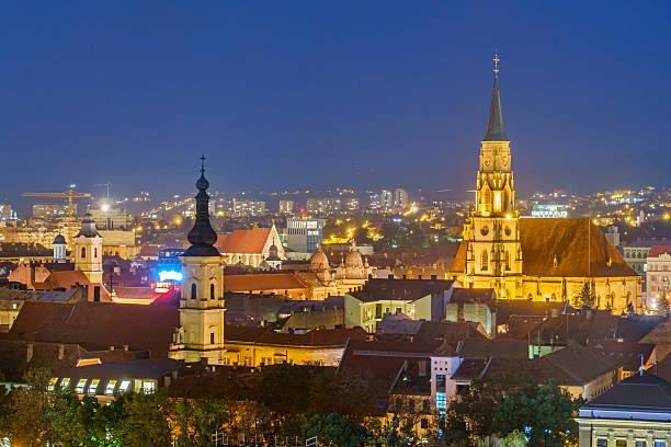 Photo of the downtown cityscape and church spires in Cluj Napoca, Transylvania, Romania at twilight blue hour, night.