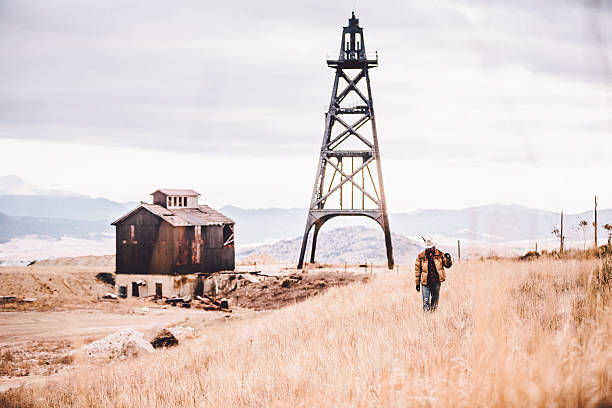 istock Man carrying pickaxe walking by old oil drill and barn 500613199