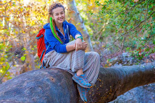 alegre menina com mochila sentado em roupas de estilo hippie floresta - hippie women dreadlocks human hair - fotografias e filmes do acervo