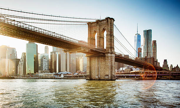 Brooklyn bridge from East river sunset with flare Brooklyn bridge from East river at sunset with flare. Wall street area, Freedom tower and the Beekman tower are seen behind it. brooklyn bridge photos stock pictures, royalty-free photos & images