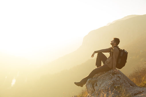 Male hiker sitting alone on a mountain top, enjoying the peace and quiet of a nature.