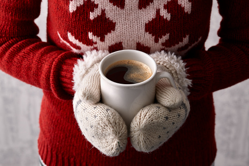 Woman hands in cute christmas mittens holding a cup of coffee