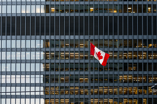 Canadian flag in front of a modern office building at dusk downtown Toronto, with illuminated office spaces.