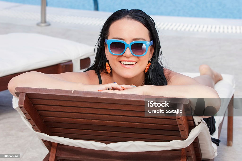 Woman sunbathing by pool Happy young woman in swimsuit lying on chaise longue poolside Adult Stock Photo