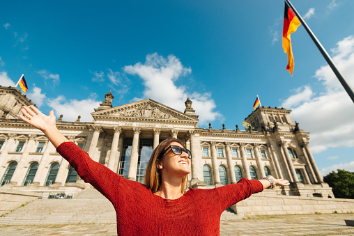 Happy young woman in spring raises her arms in front of Bundestag - Parliament of Federal Republic of Germany. Image taken with Nikon D800 and 16-35mm pro lens, developed and processed from RAW and distributed in XXXL size. Location: Berlin, Germany