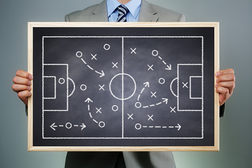 Business strategy businessman holding a blackboard planning team strategy on a chalk drawing of a soccer playing field