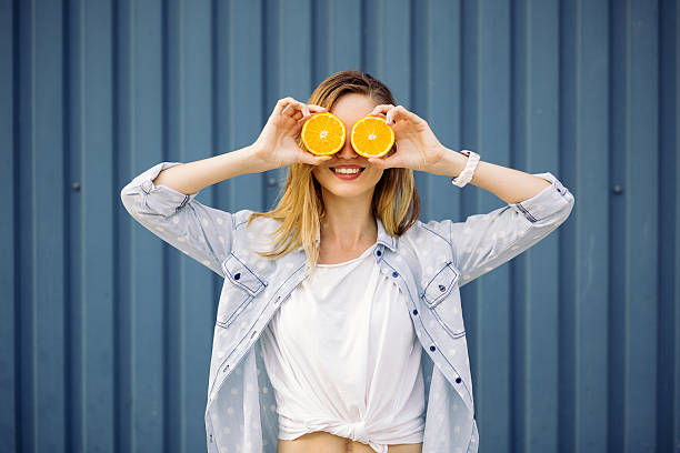 Smiling woman holding two orange in hands Smiling woman holding two grapefruits in hands on a blue background oranges with faces stock pictures, royalty-free photos & images