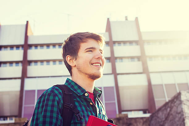istock University.Smiling young student man holding a book and a bag 500704190