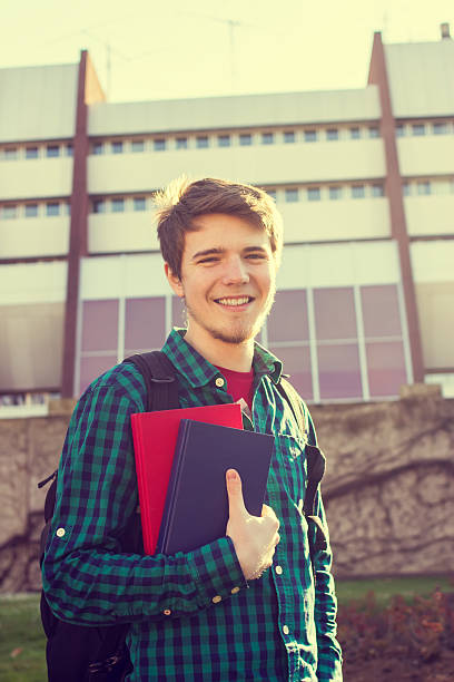 istock University.Smiling young student man holding a book and a bag 500704232
