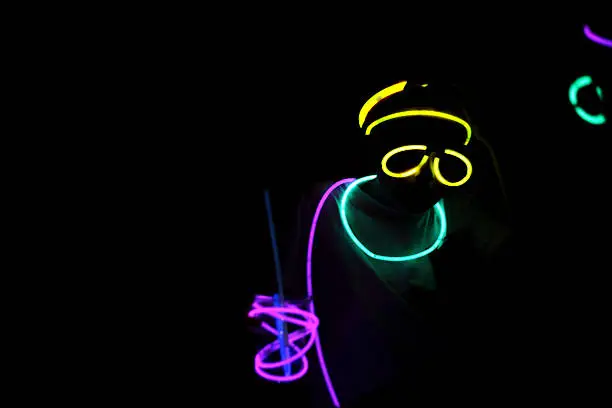 Person wearing colorful neon glow sticks at night; Copy space