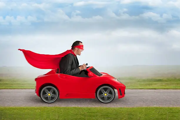 Photo of superhero man driving a toy racing car