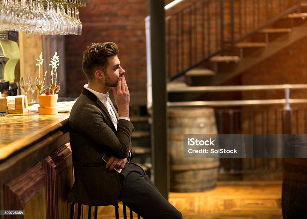 Stood Up A young man is dressed smarty at a bar waiting, he looks fed up as if he has been stood up on a date. One hand is on his face and the other is holding his smart phone. Men Stock Photo