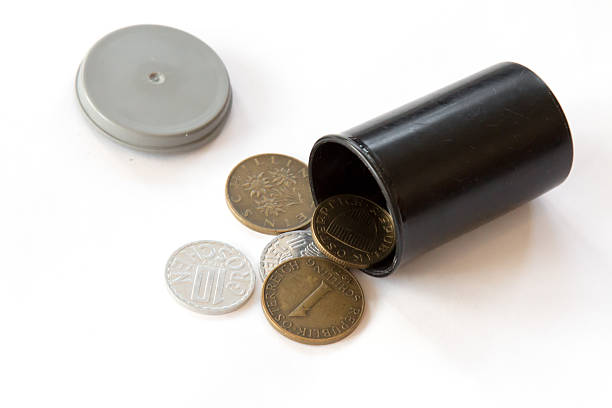 Image of obsolete Austrian coins spilling out of a plastic film canister from a bygone era.  The container is being used to store the schillings.  The film container and coins are set on a white background.