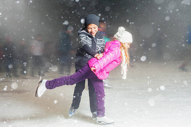 Happy children ice skating at ice rink outdoor, figure skating, at winter snowy night, sport and healthy lifestyle, ice skating at Holland. Funny kids, boy and girl, sister and brother. Family