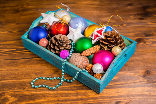 vintage wooden box with Christmas decoration, tinsel,  pinecones, stars and balls on wooden background, closeup