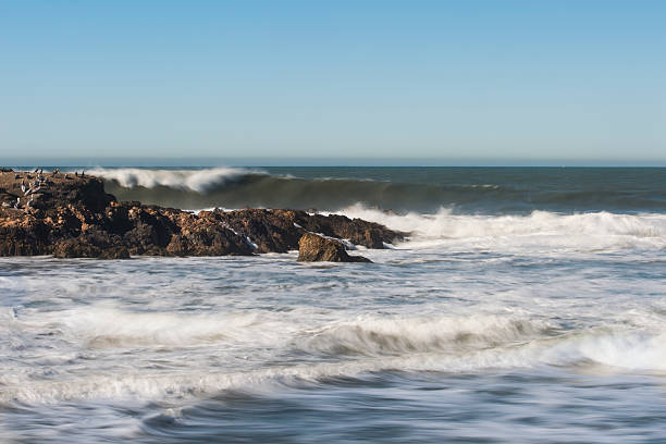 Waves crashing colorful rocks with green algae on the shore in Spain