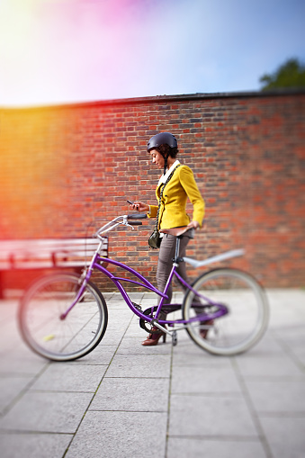 Young woman commuting by bicycle in London and writing a text message on her smart phone.
