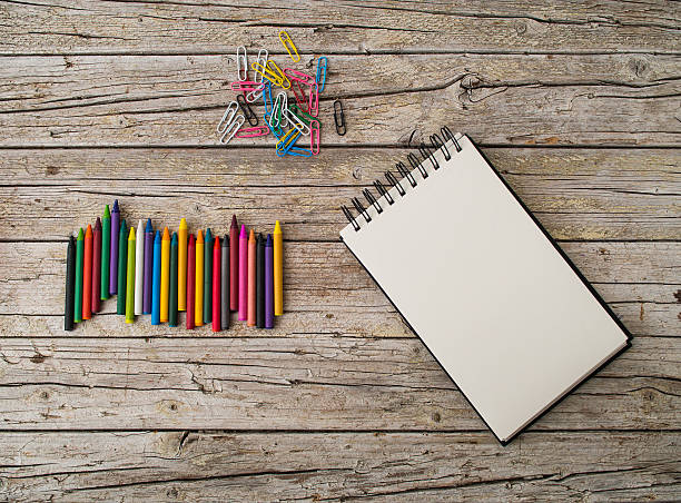 istock Wax pencils, paper clips and notebook on wooden background 500754450