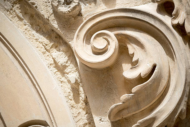 A decorative stucco frame featuring elegant classical ornaments, including cornucopias and a shell motif, on a light yellow wall