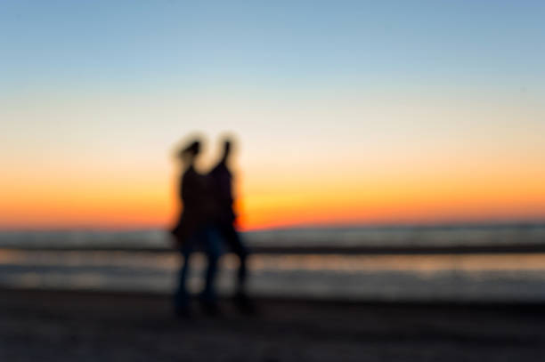 deux personnes flou silhouettes marchant le long de la plage au coucher du soleil - shadow focus on shadow women sunset photos et images de collection