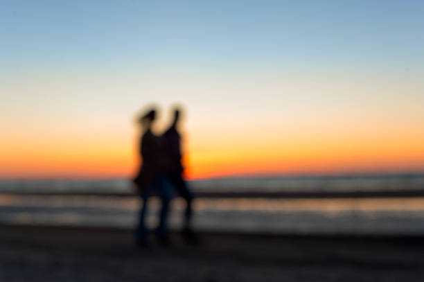 due persone sfocati linee a piedi lungo la spiaggia al tramonto - shadow focus on shadow women sunset foto e immagini stock