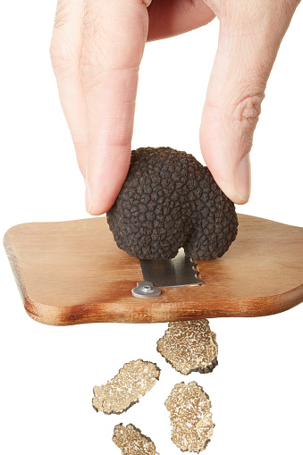 Hand slicing black truffle with wooden truffle slicer isolated on white, clipping path included