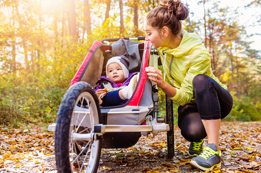 Beautiful young mother with her daughter in jogging stroller running outside in autumn nature