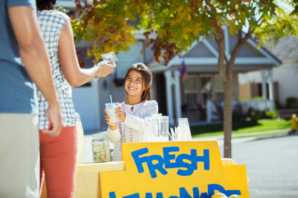 Little girl selling lemonade from a lemonade stand outdoors in summer to children