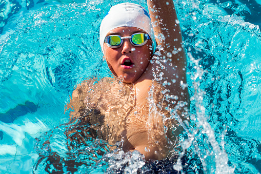 Close up action portrait of teen boy swimming backstroke.Top view of young swimmer with cap and goggles.