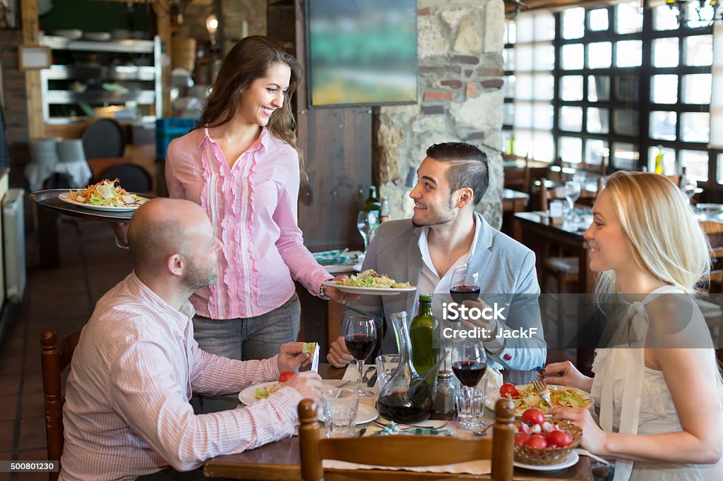Waiter with restaurant guests at table Young female waiter serving restaurant guests. Selective focus 2015 Stock Photo