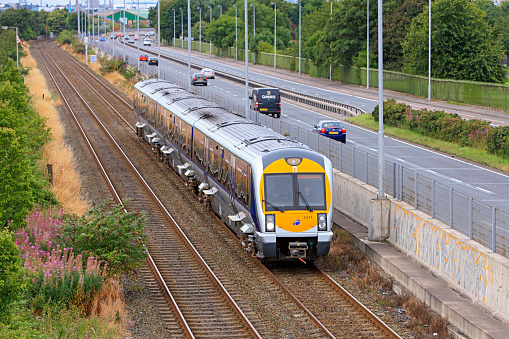Belfast, United Kingdom - August 6, 2011: A modern commuter train from Belfast Central operated by Northern Ireland Railways (NIR) for Translink slows on approach to a suburban station.  Alongside the double-track railway runs the four-lane A2 Sydenham By-pass highway, complete with an iconic Guinness truck!
