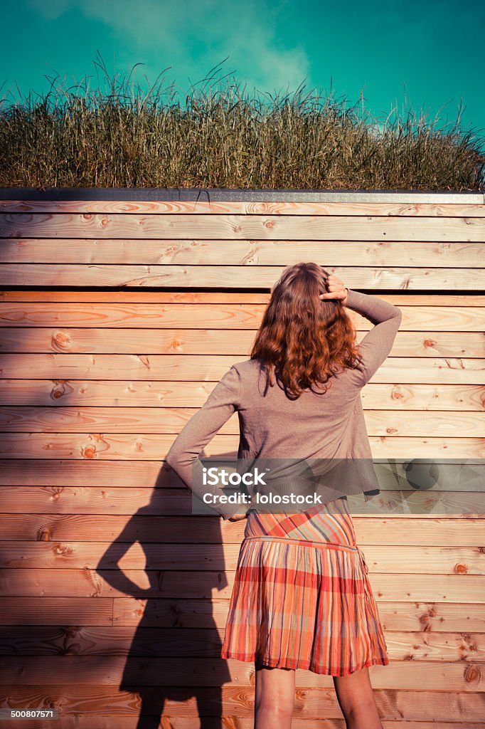 Young woman standing in garden outside cabin A young woman is standing in a garden outside a woden cabin and is looking up Adult Stock Photo