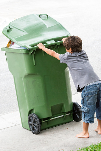 Child moving a wheeled trash can 
