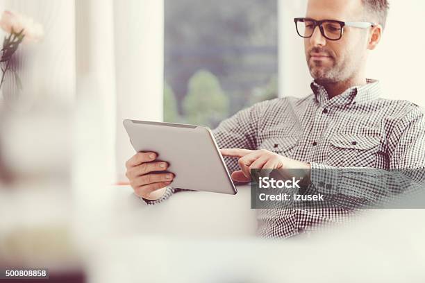 Hombre Usando Una Tableta Digital En Su Hogar Foto de stock y más banco de imágenes de Tableta digital - Tableta digital, Leer, Lector de libros electrónicos