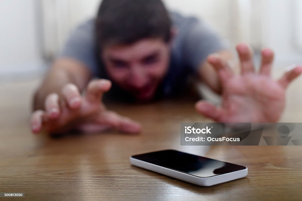 man creeping on ground smart phone and internet addiction concept young man in shallow depth of focus trying to reach mobile phone terminal creeping on the ground in smart phone and internet addiction concept Reaching Stock Photo